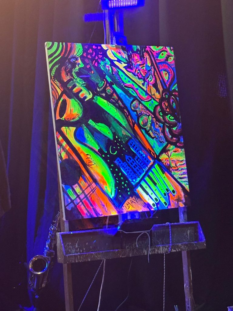 El pasado martes 23/07 en Sala Camacuá se produjo el octavo concierto organizado por el Club del Blues en una interesante iniciativa que consiste en traer a consagrados y veteranos artistas del blues norteamericano para tocar con una banda soporte local. En la previa se presentaron en dúo Clara Lassus y Junior Flores, y luego La Máquina a Vapor como teloneros, haciendo clásicos con sus dinámicos y acostumbrados cambios de instrumentistas y artistas sobre el escenario. Nunca decepcionan. El escenario lució renovado telón y la iluminación estuvo a cargo de Guillermo Ifrán. Con entradas agotadas en una sala colmada de público multigeneracional (hasta familiar) y también inclusivo, se apersonó Michael Dotson presentado como "el blues de Chicago que ya no se toca en Chicago", soportado por Adrián Flores en batería, Hernán Poloni en guitarra y Junior Flores en bajo. Ante una audiencia rendida a sus pies, tocó y cantó durante más de una hora, generando momentos de tensa intimidad y también picos de euforia. No soy cronista musical por lo tanto no voy a tener el atrevimiento de comentar en ese aspecto, pero el show claramente fue muy satisfactorio para el público que festejaba cada comentario (volaban las traducciones simultáneas susurradas), al mismo tiempo que a un costado del escenario un colectivo de artistas plásticos iba generando una obra pictórica en tiempo real, con el buen tino de incorporar pintura fluorescente, adecuadamente iluminada. Finalizó con bises sumando a los artistas locales, a toda fiesta. Un gran concierto en suma, evento multisensorial, en una sala cómoda, accesible, con baños renovados y expendio de bebidas que se pueden llevar a la sala para acompañar debidamente el espectáculo con la promesa de luego retornar los vasos y colaborar con la limpieza. Evento que ya no es el secreto mejor guardado de la escena musical montevideana, como evidenciaba la larga cola al ingreso. Sigan al Club del Blues en sus redes para enterarse del próximo show, que será en setiembre y habrán anticipadas bonificadas. El pasado martes 23/07 en Sala Camacuá se produjo el octavo concierto organizado por el Club del Blues en una interesante iniciativa que consiste en traer a consagrados y veteranos artistas del blues norteamericano para tocar con una banda soporte local.En la previa se presentaron en dúo Clara Lassus y Junior Flores, y luego La Máquina a Vapor como teloneros, haciendo clásicos con sus dinámicos y acostumbrados cambios de instrumentistas y artistas sobre el escenario. Nunca decepcionan.
El escenario lució renovado telón y la iluminación estuvo a cargo de Guillermo Ifrán.
Con entradas agotadas en una sala colmada de público multigeneracional (hasta familiar) y también inclusivo, se apersonó Michael Dotson presentado como "el blues de Chicago que ya no se toca en Chicago", soportado por Adrián Flores en batería, Hernán Poloni en guitarra y Junior Flores en bajo.
Ante una audiencia rendida a sus pies, tocó y cantó durante más de una hora, generando momentos de tensa intimidad y también picos de euforia.
No soy cronista musical por lo tanto no voy a tener el atrevimiento de comentar en ese aspecto, pero el show claramente fue muy satisfactorio para el público que festejaba cada comentario (volaban las traducciones simultáneas susurradas), al mismo tiempo que a un costado del escenario un colectivo de artistas plásticos iba generando una obra pictórica en tiempo real, con el buen tino de incorporar pintura fluorescente, adecuadamente iluminada.
Finalizó con bises sumando a los artistas locales, a toda fiesta.
Un gran concierto en suma, evento multisensorial, en una sala cómoda, accesible, con baños renovados y expendio de bebidas que se pueden llevar a la sala para acompañar debidamente el espectáculo con la promesa de luego retornar los vasos y colaborar con la limpieza.
Evento que ya no es el secreto mejor guardado de la escena musical montevideana, como evidenciaba la larga cola al ingreso.
Sigan al Club del Blues en sus redes para enterarse del próximo show, que será en setiembre y habrán anticipadas bonificadas.