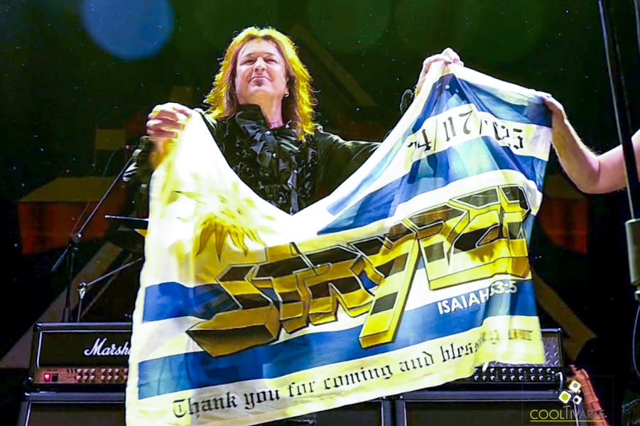 Una persona sostiene una bandera de uruguay con el estanpado escrito de STRYPER